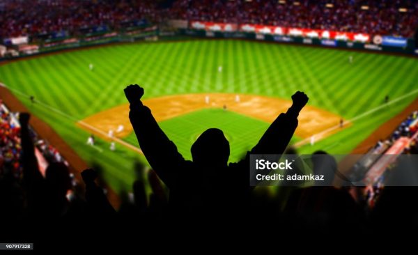 A baseball fan raises his arms in celebration. The stadium is fictional.